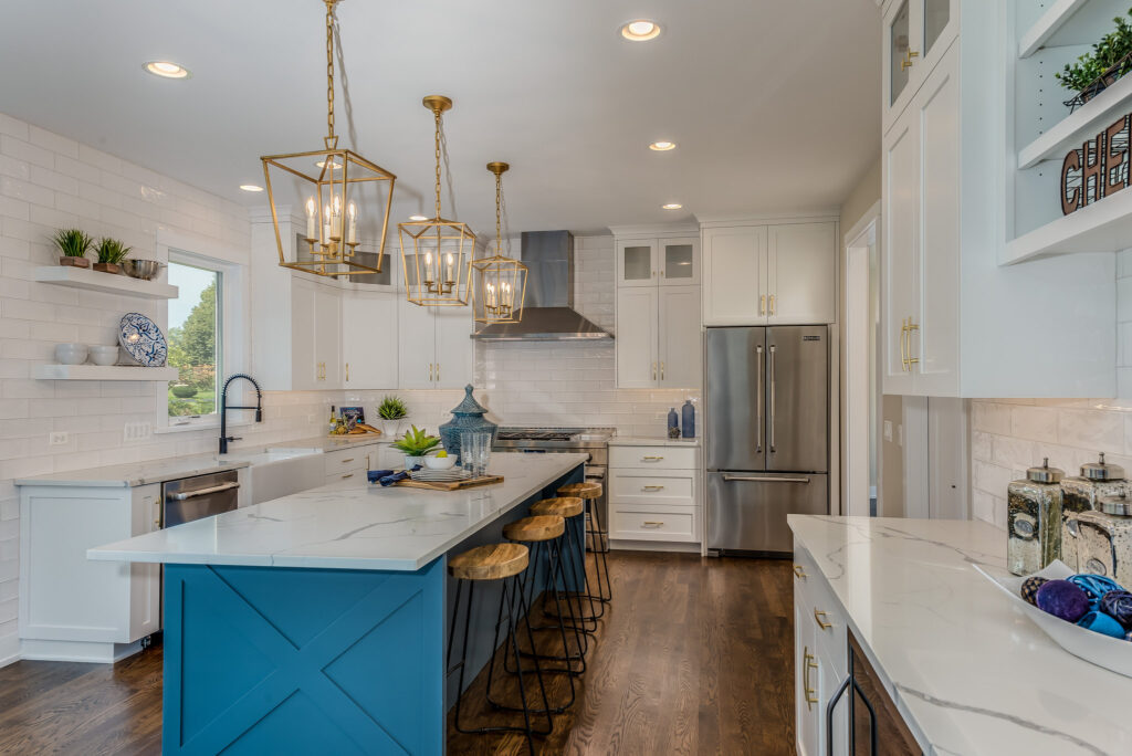 Bright white shaker kitchen with teal X-panel island, quartz countertops, and brass lantern pendants in Calabasas by RnD Builders Inc