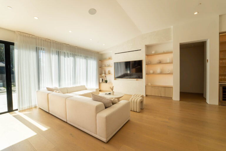 Bright open living room with white sectional, oak hardwood floors, and built-in shelving by RnD Builders Inc