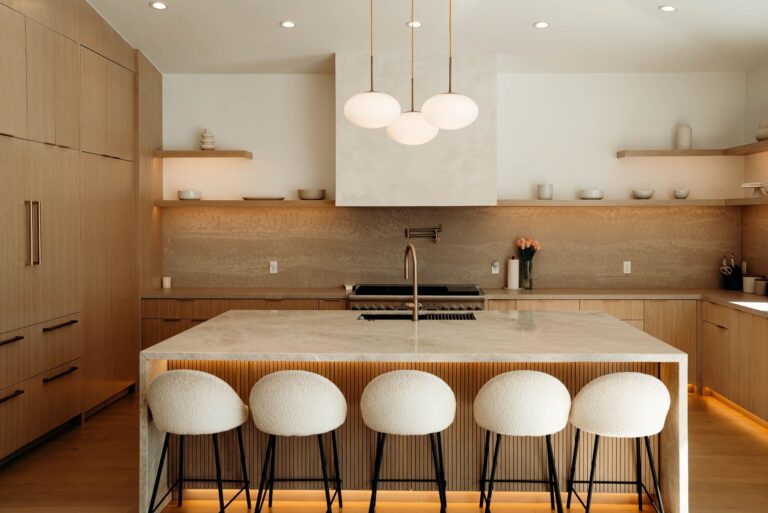 Warm modern kitchen with flat-panel oak cabinets, stone slab island, and bouclé barstools in Woodland Hills by RnD Builders Inc