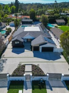 default Aerial view of modern single-story home with dark shingle roof, three-car garage, solar panels, and backyard pool by RnD Builders Inc