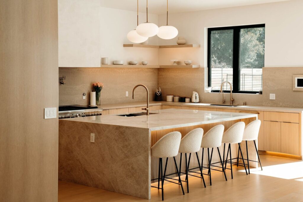 Warm Modern Kitchen with Stone Waterfall Island in Woodland Hills Warm modern kitchen with stone waterfall island, flat-panel oak cabinets, and boucle counter stools in Woodland Hills by RnD Builders Inc
