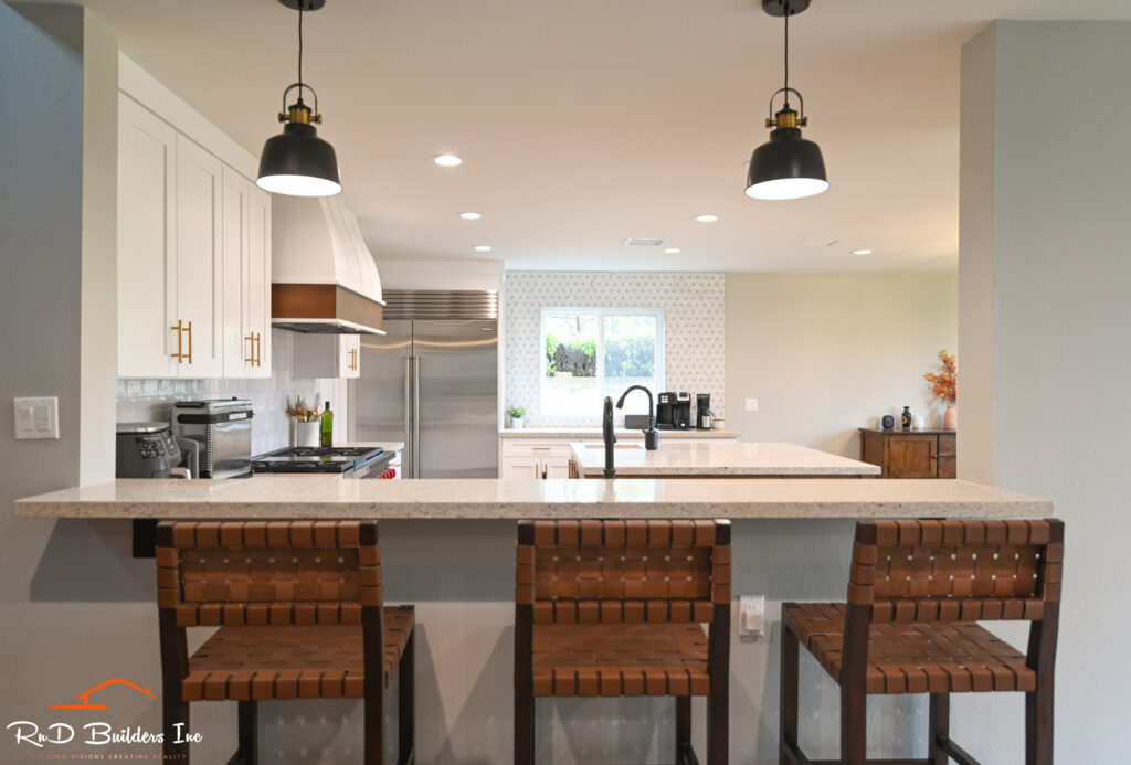 White Shaker Kitchen with Quartz Island Newbury Park home remodel: White shaker kitchen with quartz island, custom range hood, and woven leather barstools in Newbury Park by RnD Builders Inc