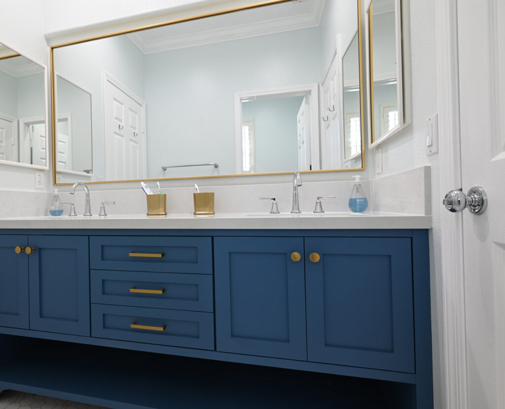 Double-sink Bathroom Vanity with Navy Blue Shaker Cabinets Double-sink bathroom vanity with navy blue shaker cabinets, white quartz countertop, and gold-framed mirrors by RnD Builders Inc