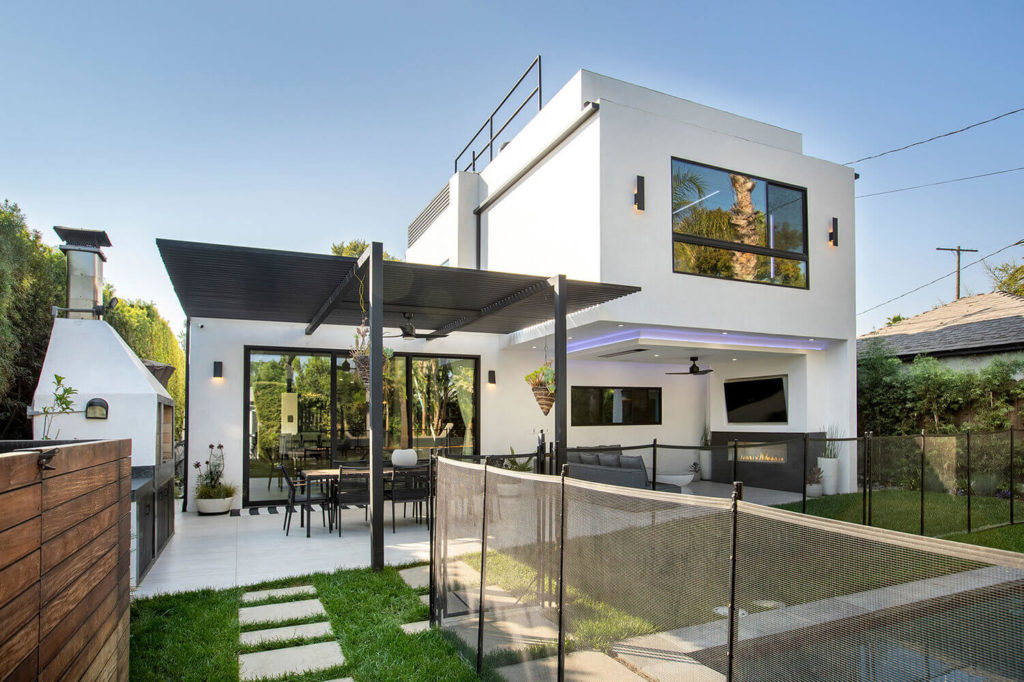 Modern two-story white stucco home with black pergola, outdoor lounge, and pizza oven by RnD Builders Inc