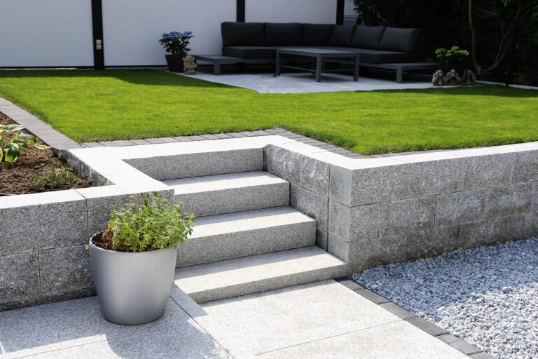 Neat and tidy garden with granite wall and solid block steps Modern backyard with granite retaining wall, stone steps, paver patio, and manicured lawn by RnD Builders Inc