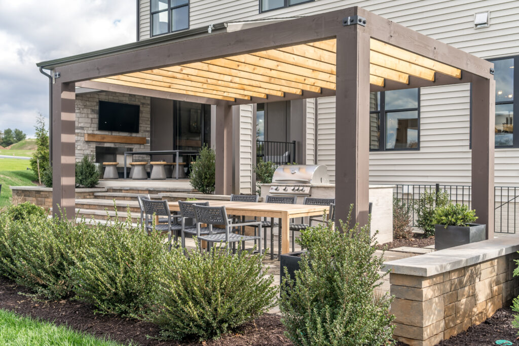 RnD - Exterior2 Modern outdoor patio with pergola, dining set, stainless grill, and stone fireplace by RnD Builders Inc