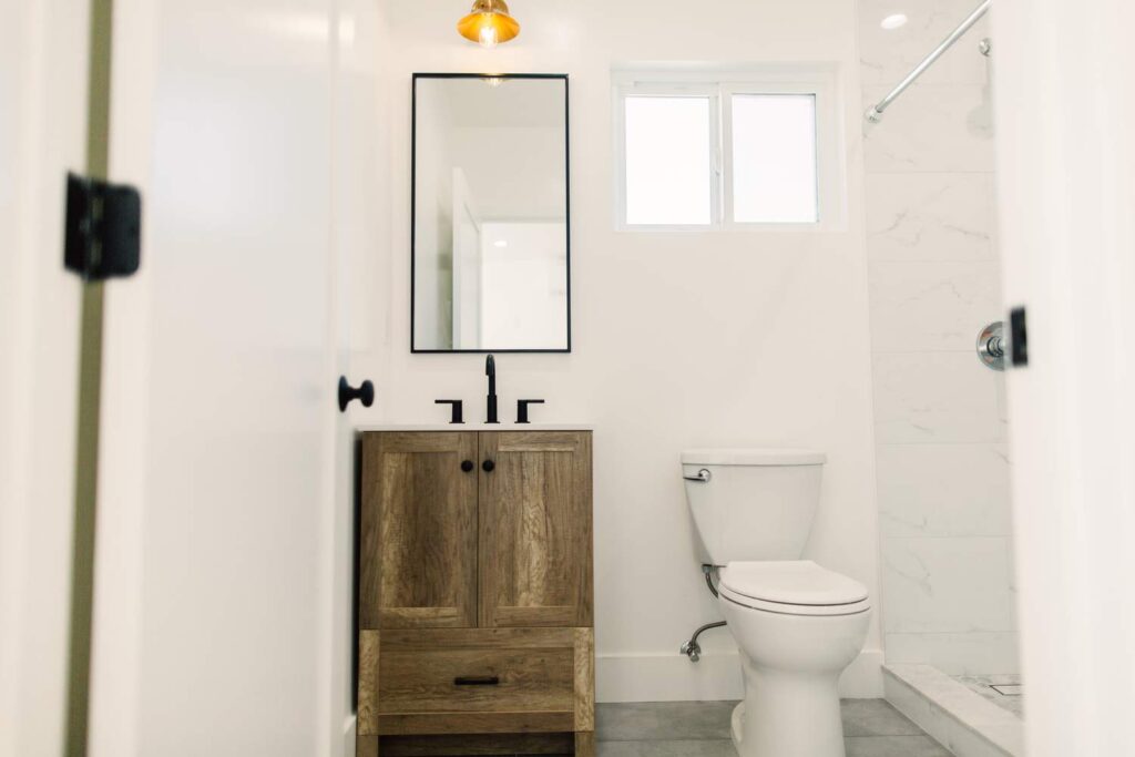 Modern Farmhouse Bathroom with Rustic Wood Vanity in Hawthorne Modern farmhouse bathroom with rustic wood vanity, black fixtures, and marble-look tile shower in Hawthorne by RnD Builders Inc