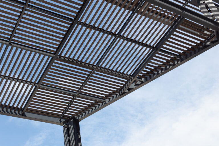 Upward view of modern pergola with wood slat lattice roof and steel frame by RnD Builders Inc