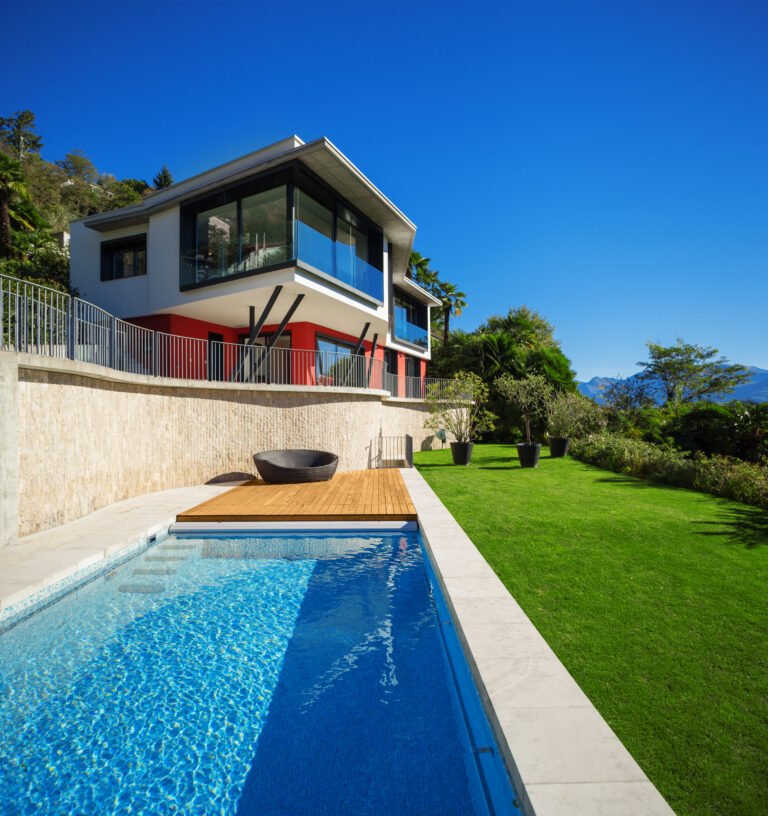 Modern two-story home with glass railings, lap pool, wood deck, and landscaped lawn by RnD Builders Inc