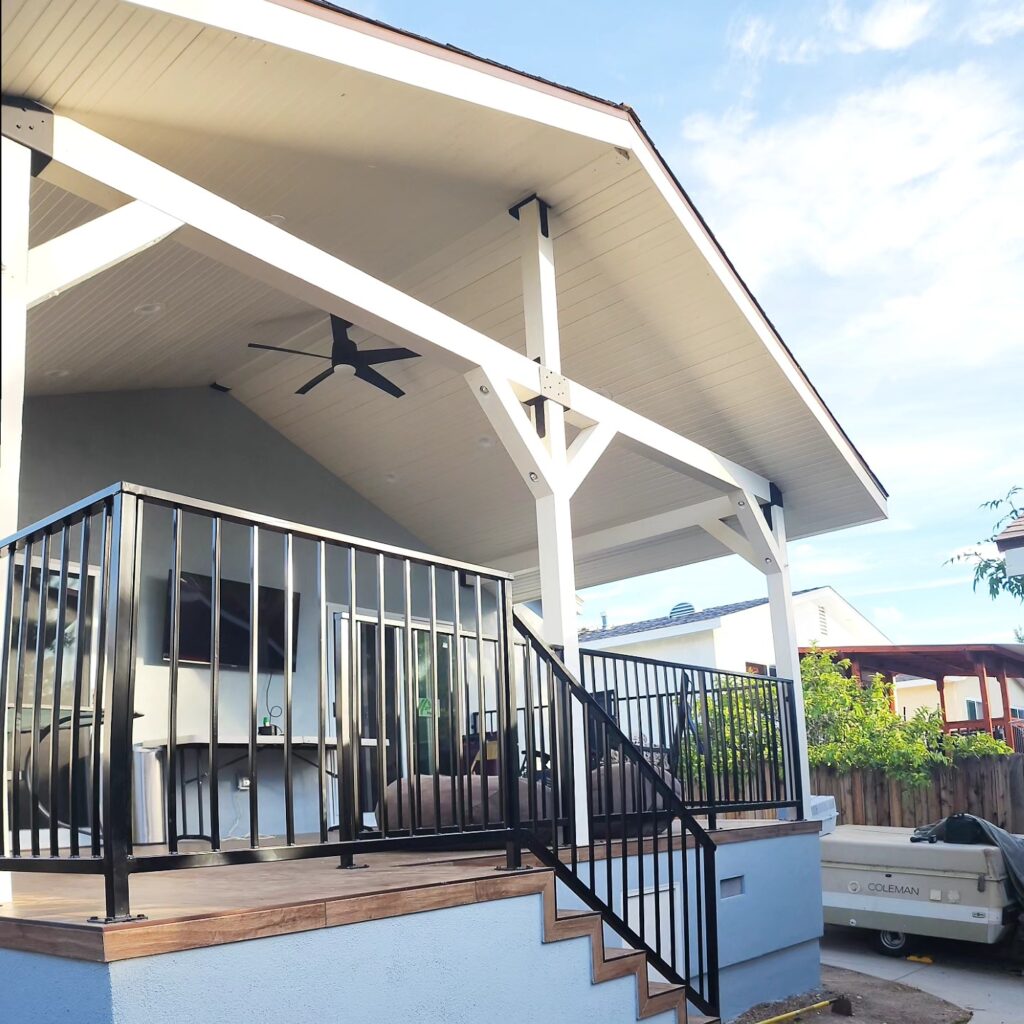 Covered outdoor deck with gabled roof, black ceiling fan, and metal railing by RnD Builders Inc
