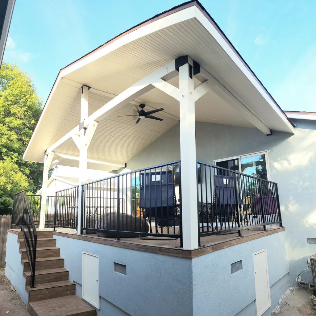 Covered Outdoor Deck with Gabled Roof Covered outdoor deck with gabled roof, ceiling fan, black iron railings, and wood stair treads by RnD Builders Inc