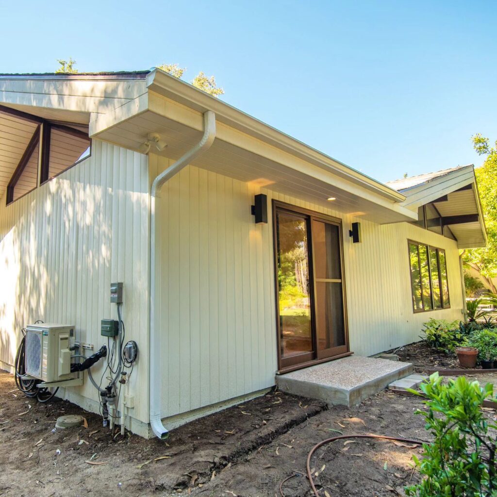Exterior Addition with Cream Vertical Board Siding Exterior addition with cream vertical board siding, sliding glass door, and mini-split HVAC unit by RnD Builders Inc