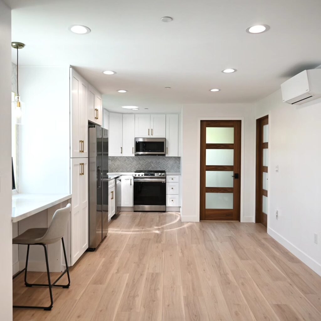 Bright ADU Kitchen with White Shaker Cabinets Bright ADU kitchen with white shaker cabinets, herringbone backsplash, and light hardwood floors by RnD Builders Inc