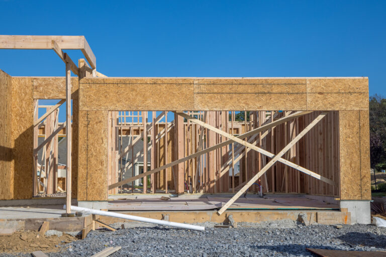 wooden natural house construction against the sky Residential new construction wood framing with OSB sheathing and stud walls under blue sky by RnD Builders Inc