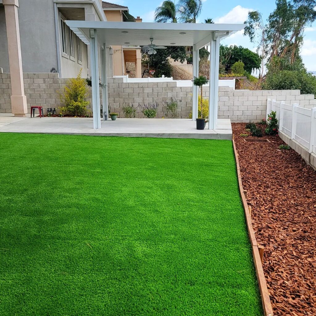 Backyard landscaping with artificial turf, concrete patio, white aluminum patio cover, and block wall by RnD Builders Inc