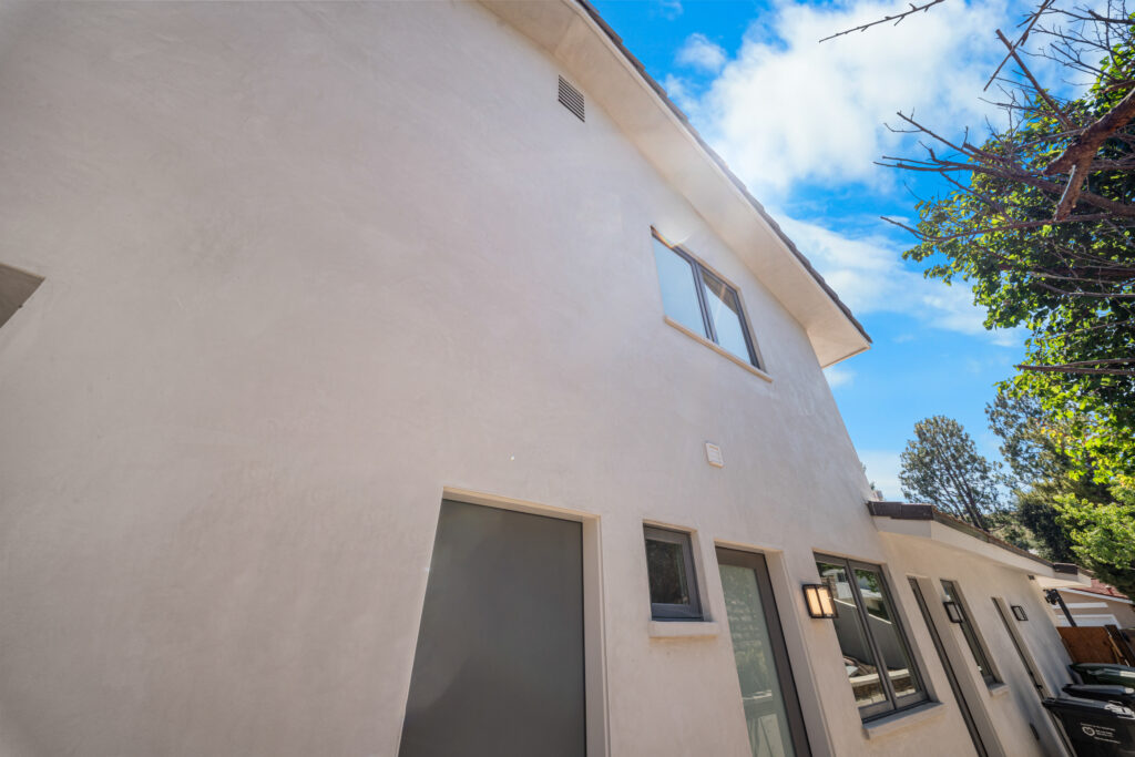 Two-story stucco exterior with dark-framed windows and modern wall sconce by RnD Builders Inc