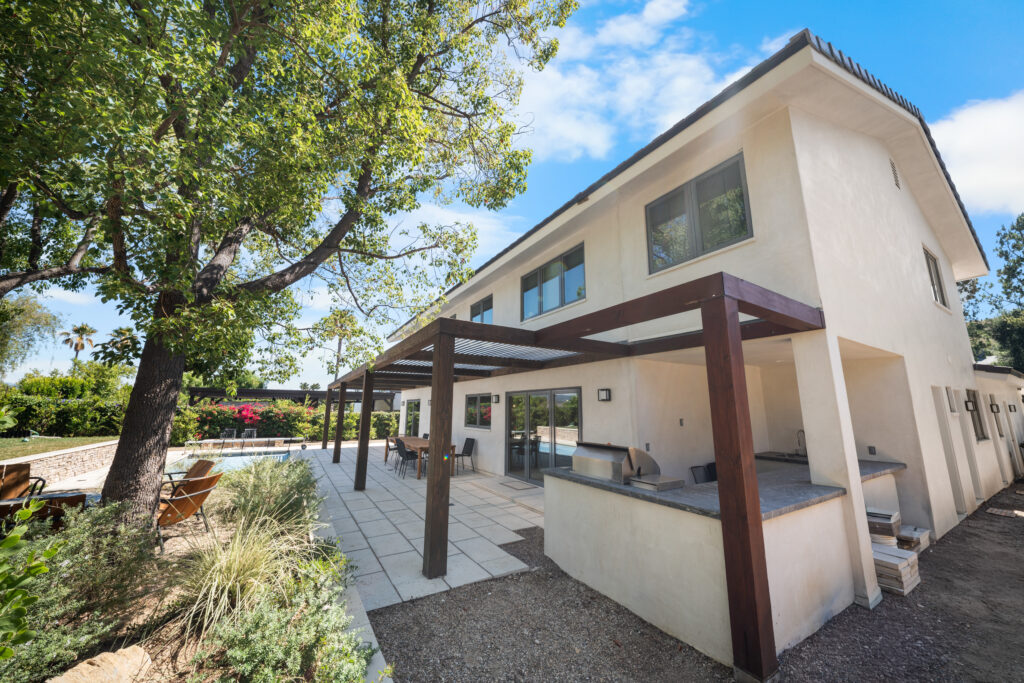 Two-story stucco home exterior with pergola, outdoor kitchen, and pool by RnD Builders Inc