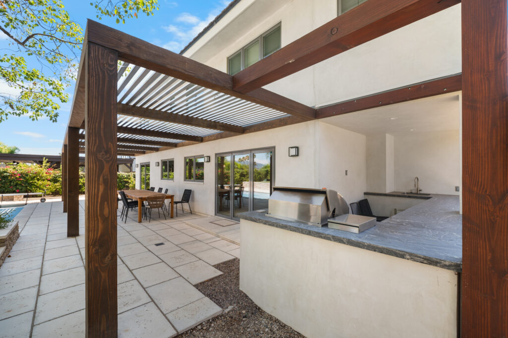 Outdoor kitchen and pergola patio with stainless grill, granite countertop, and wood beams by RnD Builders Inc