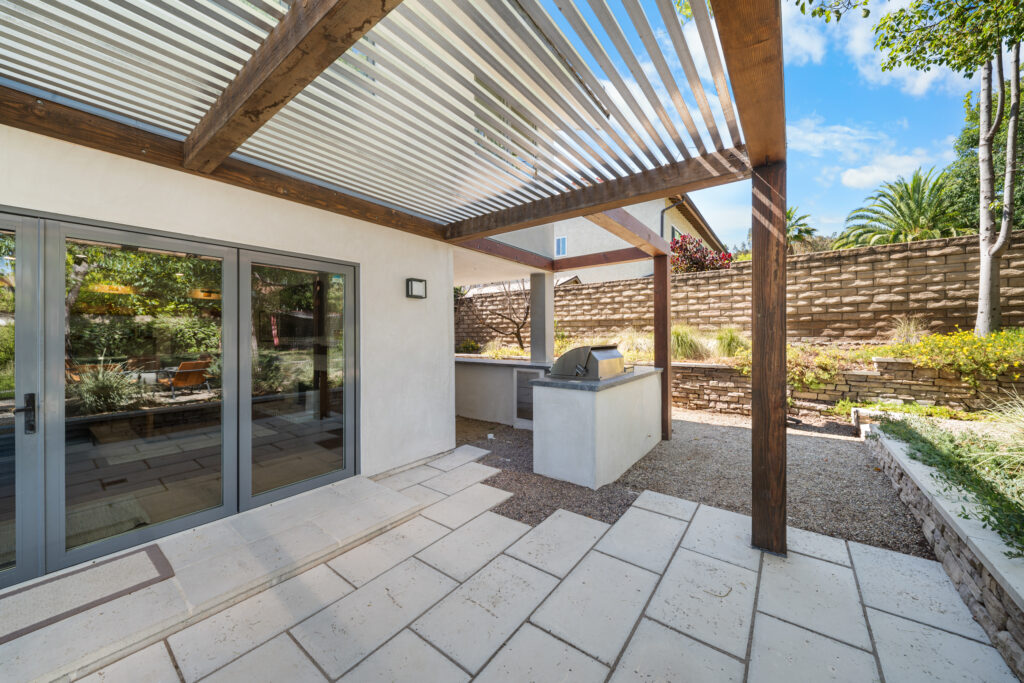 Covered outdoor patio with wood pergola, built-in BBQ island, and stone pavers by RnD Builders Inc