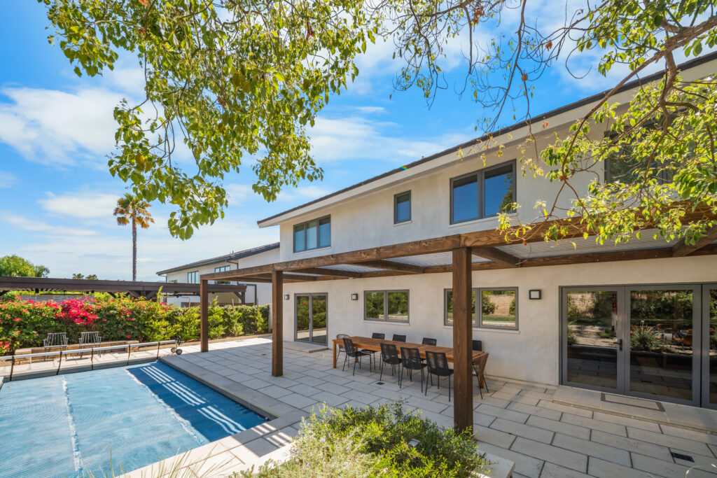 Two-story stucco home with wood pergola, patio dining set, and pool by RnD Builders Inc