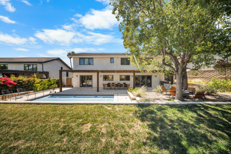 Two-story stucco home with rectangular pool, wood pergola, and patio dining area by RnD Builders Inc