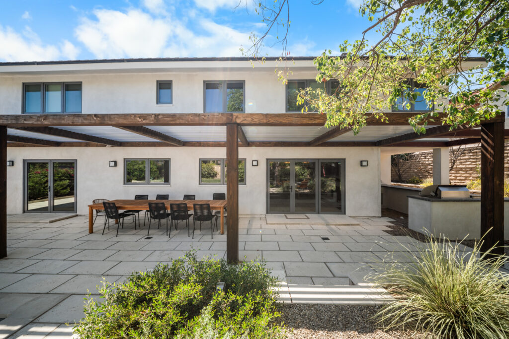 Modern two-story stucco home with wood pergola, paver patio, and outdoor dining area by RnD Builders Inc