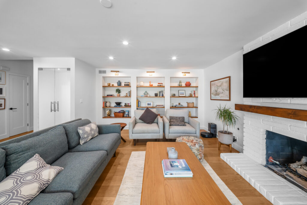 Bright living room with built-in shelving, white brick fireplace, and hardwood floors by RnD Builders Inc