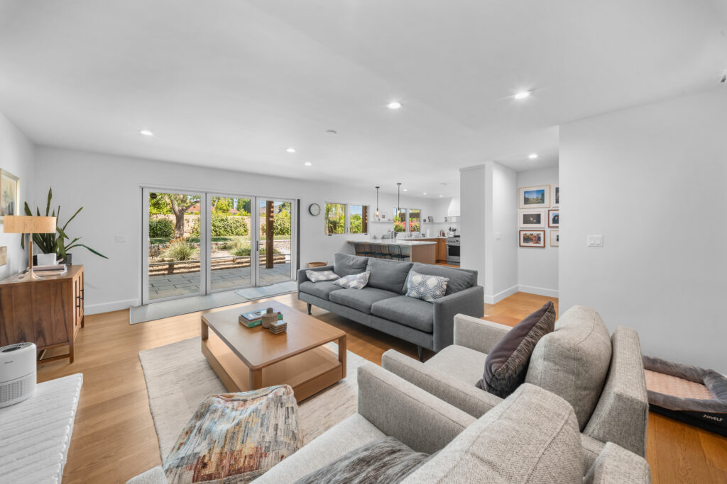 Open-concept living room with hardwood floors, gray sofas, and sliding glass doors to patio by RnD Builders Inc