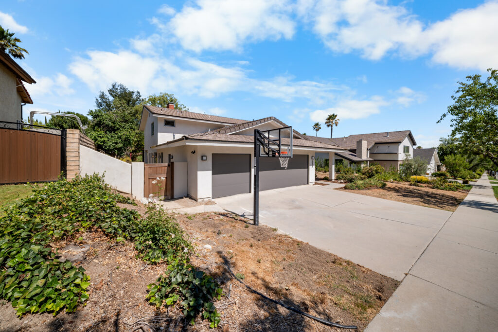 Two-story stucco home with dark gray garage doors, concrete driveway, and basketball hoop by RnD Builders Inc