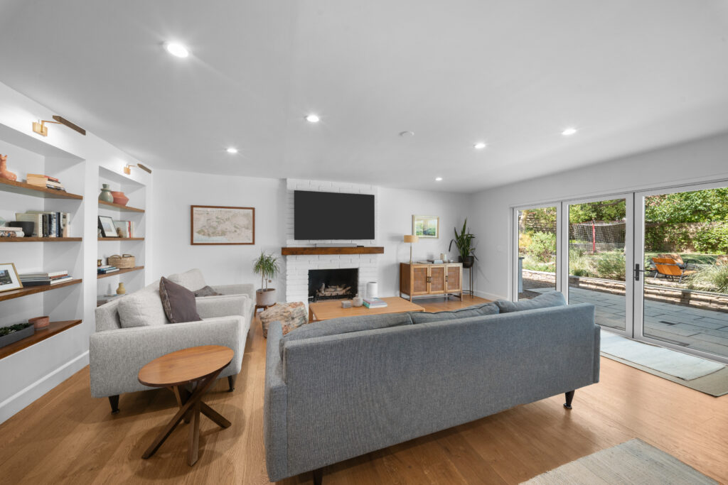 Bright open living room with white brick fireplace, built-in shelving, and sliding glass doors by RnD Builders Inc