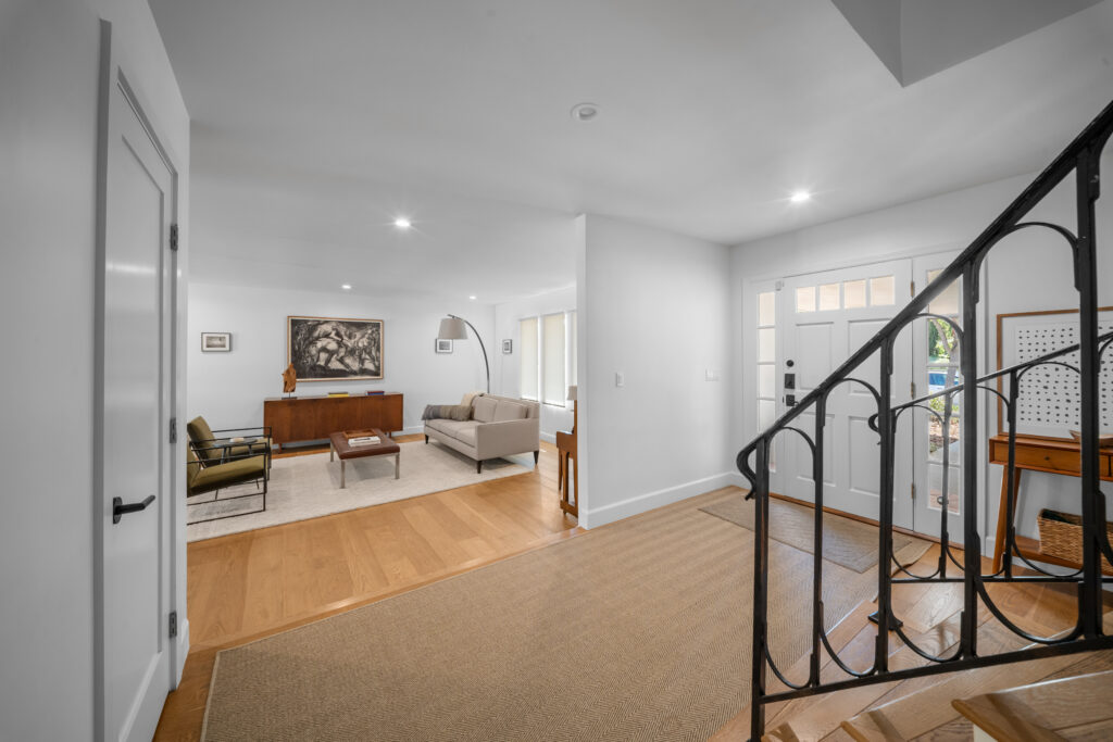 Open foyer and living room with hardwood floors and wrought iron staircase railing by RnD Builders Inc