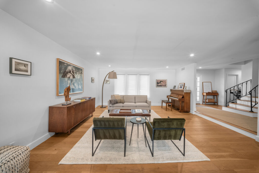 Open-concept living room with hardwood floors, mid-century furniture, and staircase by RnD Builders Inc