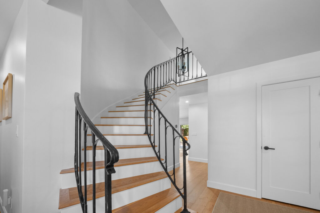 Curved staircase with wrought iron railing and hardwood treads in bright white foyer by RnD Builders Inc