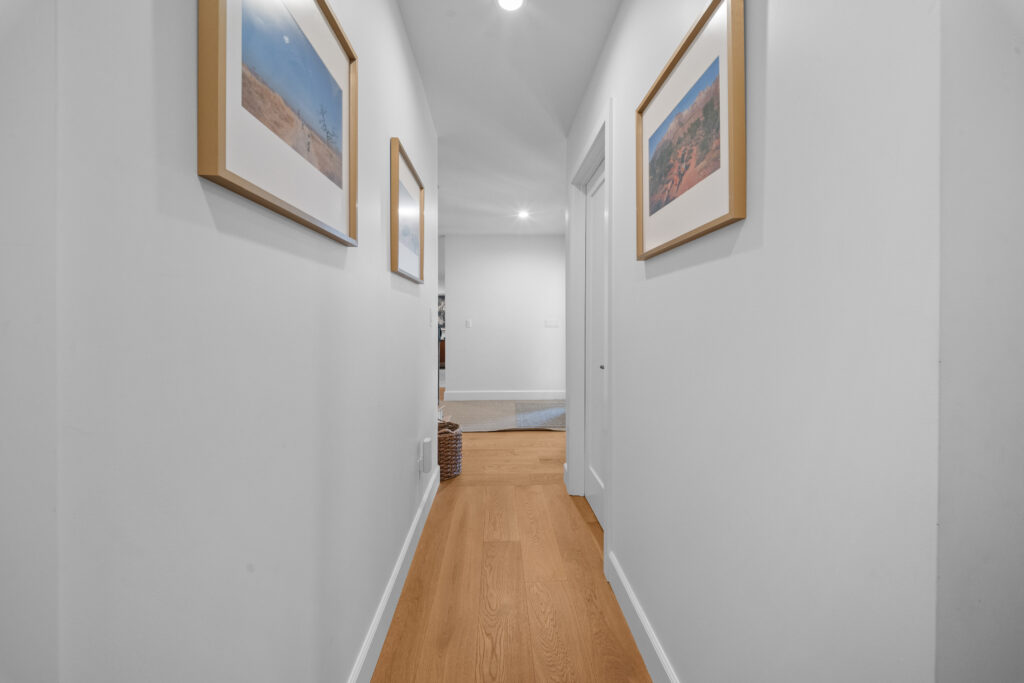 Bright residential hallway with light oak hardwood floors and framed landscape artwork by RnD Builders Inc