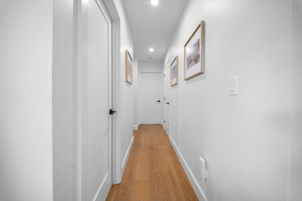 Bright residential hallway with white walls, hardwood floors, and framed artwork by RnD Builders Inc