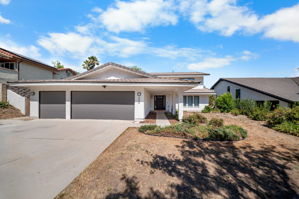 Single-story white stucco home with three-car garage and concrete driveway by RnD Builders Inc