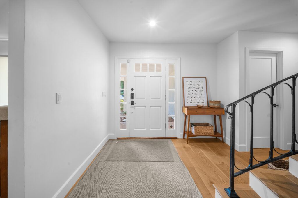 Bright residential foyer with white paneled front door, sidelights, hardwood floors, and wrought iron staircase railing by RnD Builders Inc