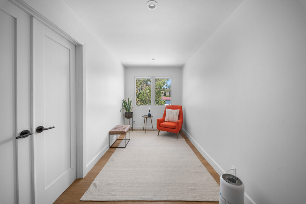 Minimalist sitting room with orange accent chair, hardwood floors, and white shaker double doors by RnD Builders Inc