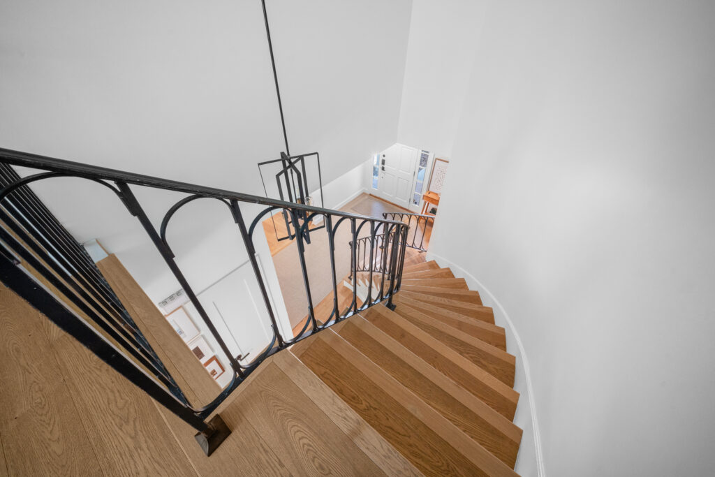 Curved staircase with oak hardwood treads and ornate wrought iron black railing by RnD Builders Inc