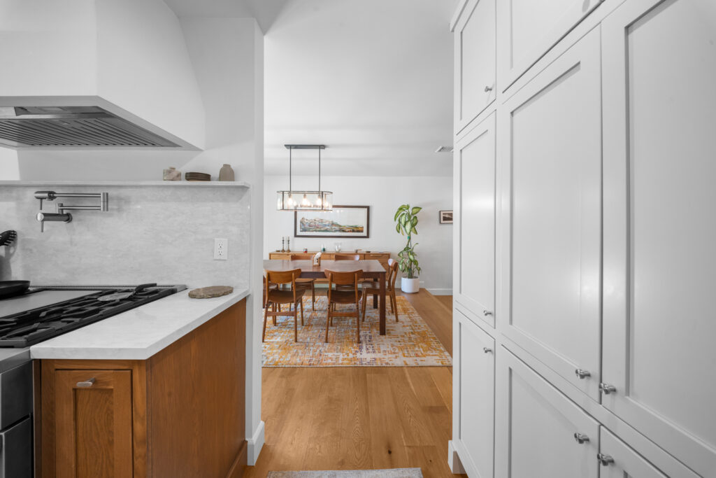 Open-concept kitchen with warm wood lower cabinets, white quartz countertops, marble backsplash, and adjacent mid-century dining room by RnD Builders Inc