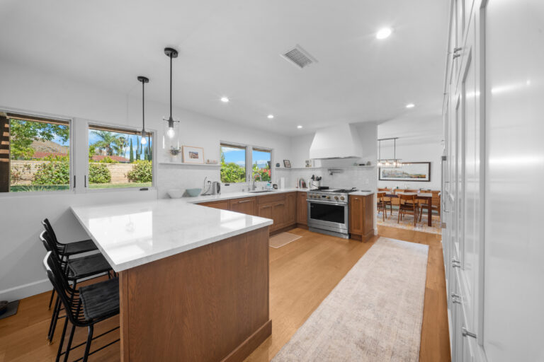 Open-concept kitchen with warm wood cabinets, white quartz island, and stainless range by RnD Builders Inc