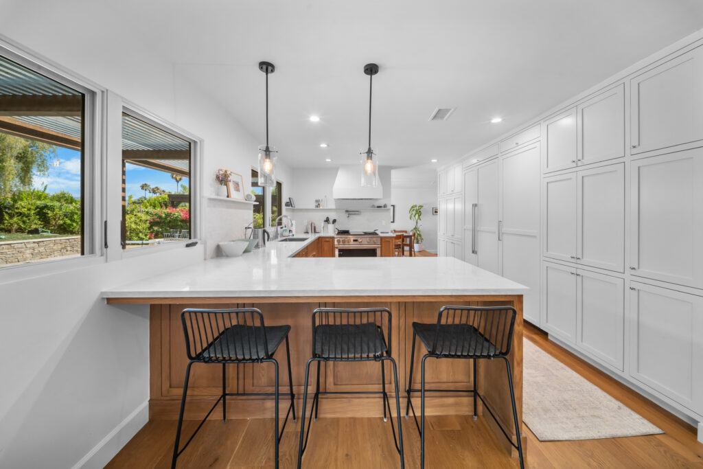 Open-concept kitchen with white quartz island, warm walnut cabinetry, and black pendant lights by RnD Builders Inc
