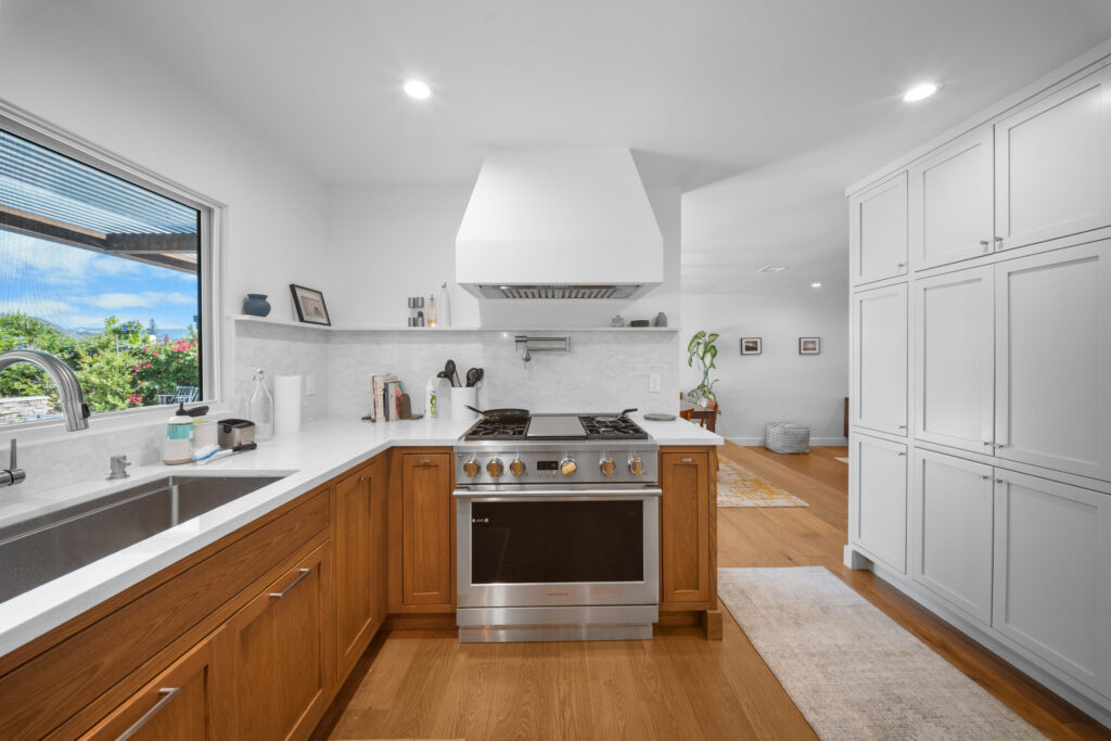 Bright kitchen with warm oak cabinets, stainless pro-range, white hood, and quartz countertops by RnD Builders Inc