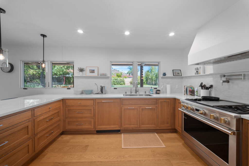 U-shaped kitchen with warm wood shaker cabinets, white quartz countertops, and stainless range by RnD Builders Inc