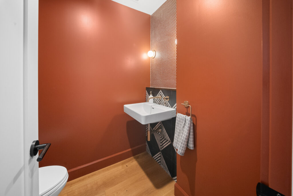 Bold terracotta powder room with wall-mount sink, penny tile backsplash, and geometric encaustic tile by RnD Builders Inc