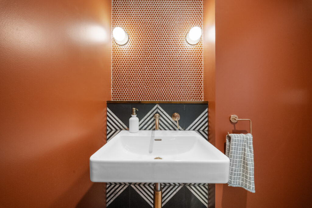 Bold powder room with terracotta penny tile backsplash, geometric patterned vanity, and white rectangular sink by RnD Builders Inc