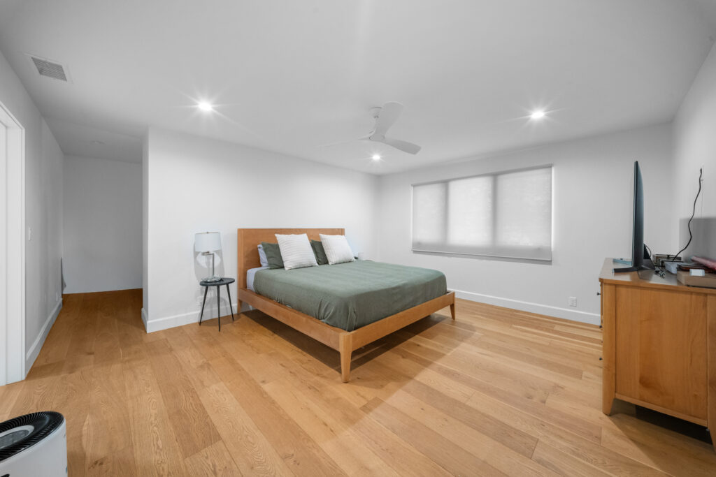 Spacious bedroom with wide-plank hardwood floors, wood-frame bed, and white ceiling fan by RnD Builders Inc