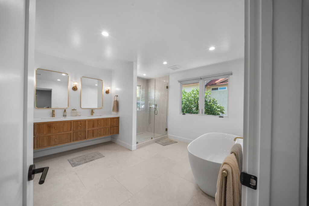 Luxury master bathroom with floating walnut vanity, freestanding soaking tub, and glass shower enclosure by RnD Builders Inc