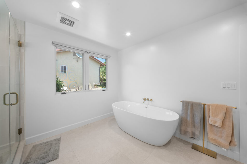 Modern master bathroom with freestanding white soaking tub and brushed gold fixtures by RnD Builders Inc