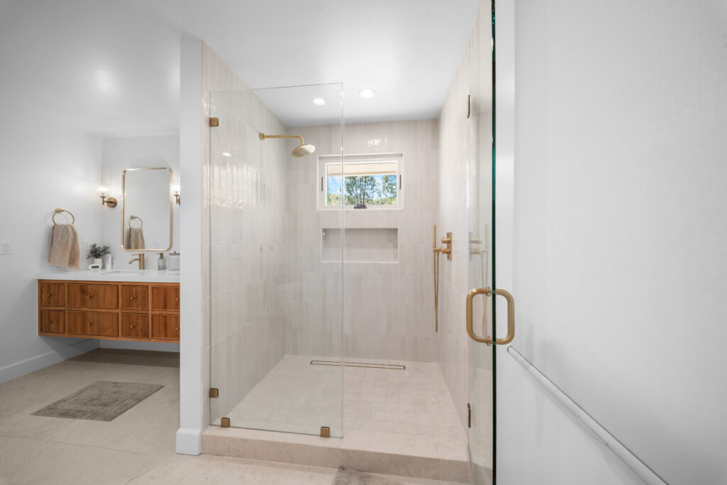 Spa-style primary bathroom with frameless glass shower and floating walnut vanity by RnD Builders Inc